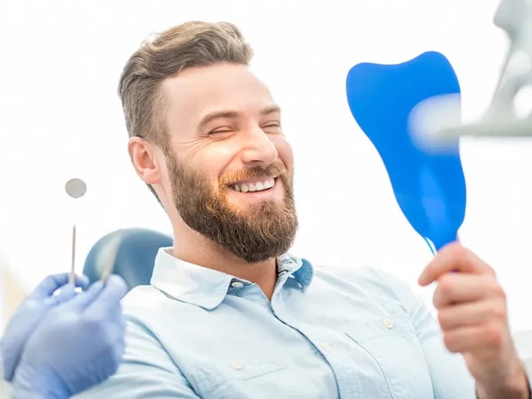 Smiling man in dental chair holding a mirror after treatment with a cosmetic dentist in Bellingham.