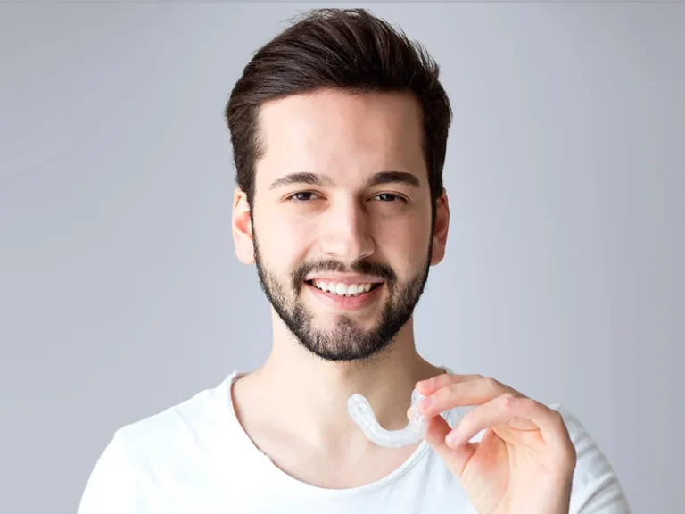 Man smiling while holding clear aligner from trusted local dentist in Bellingham.