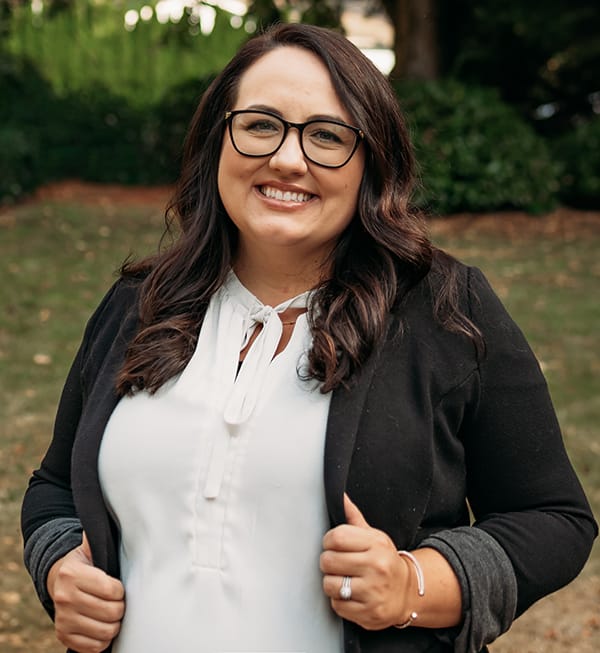 Female Roots Dental team member in Bellingham with glasses, smiling outdoors.